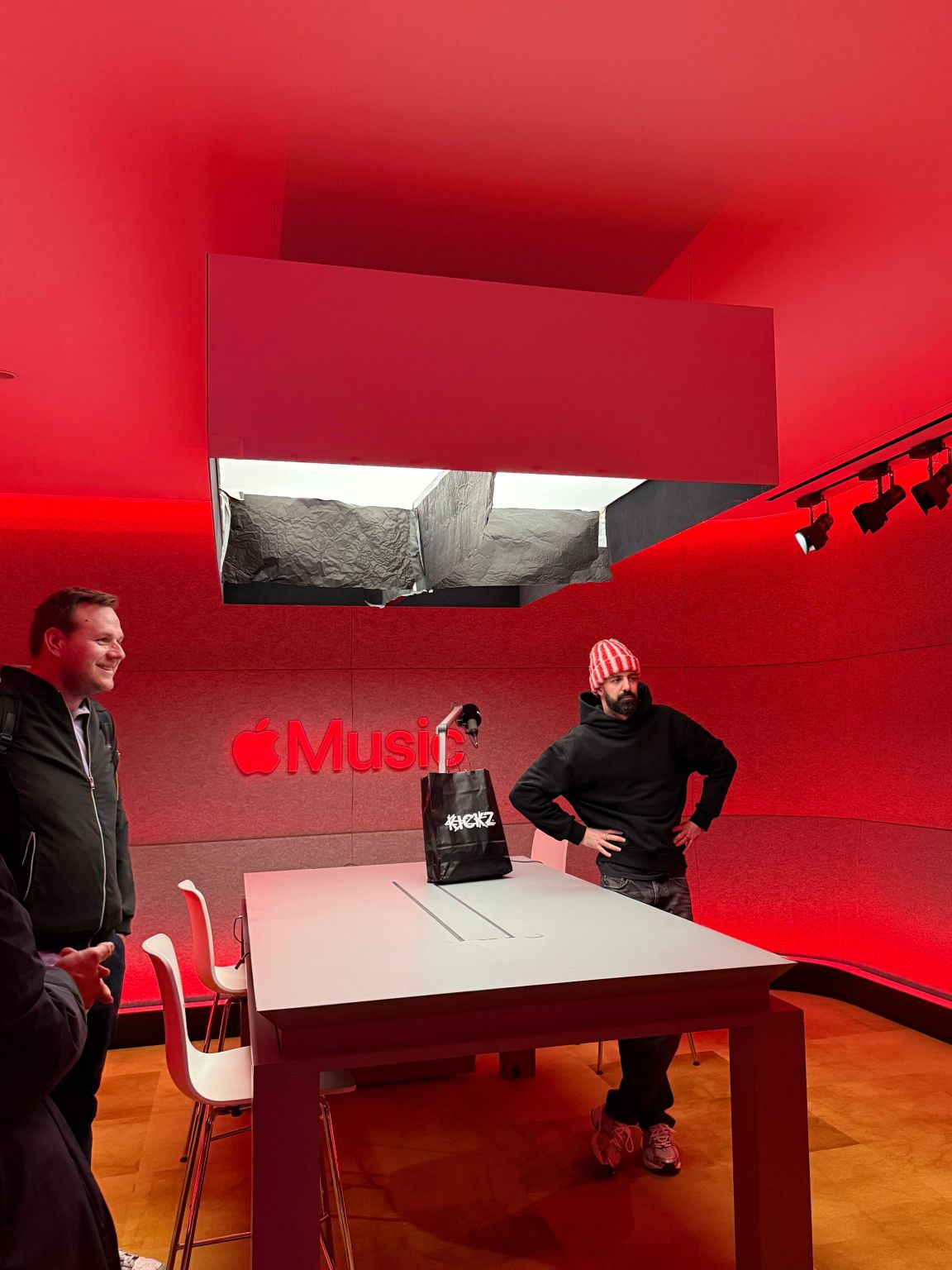 Rot beleuchteter Apple-Music-Raum mit Tisch und Mikrofon, zwei Männer bei der Aufnahme
