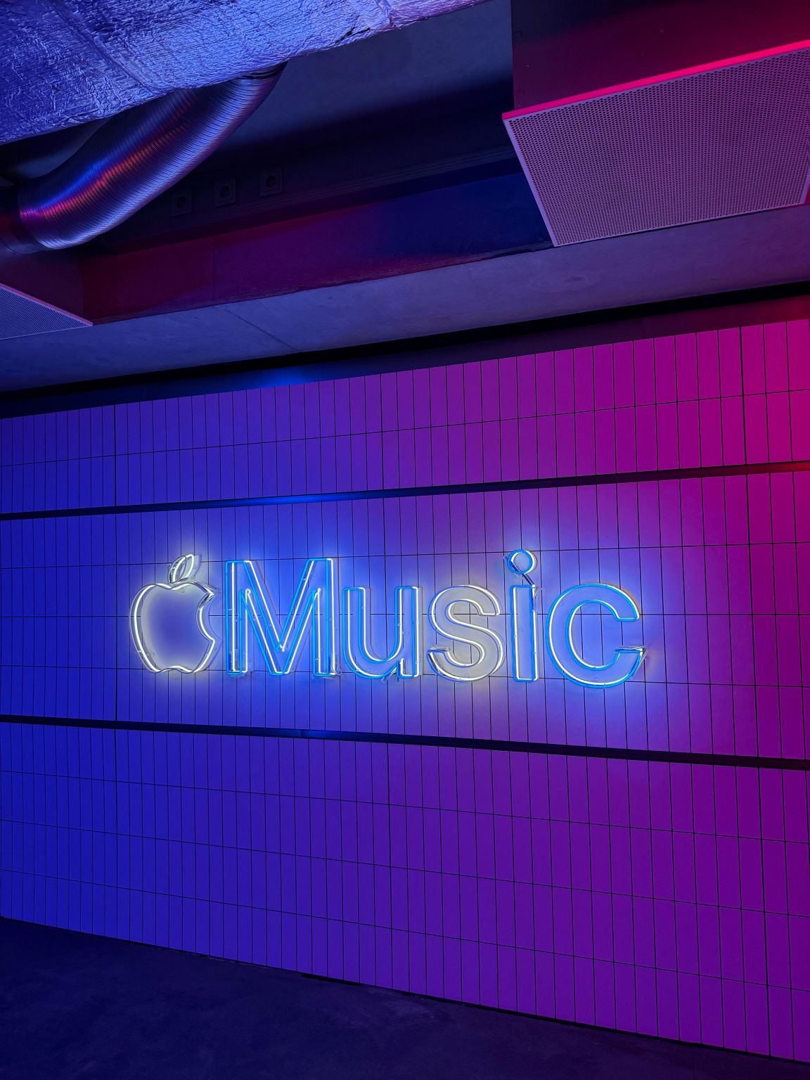Leuchtender Apple-Music-Schriftzug aus Neon an einer violett beleuchteten Fliesenwand