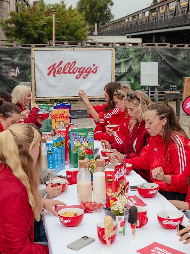 Lange Frühstückstafel mit Kellogg’s-Schalen vor Kellogg’s-Banner