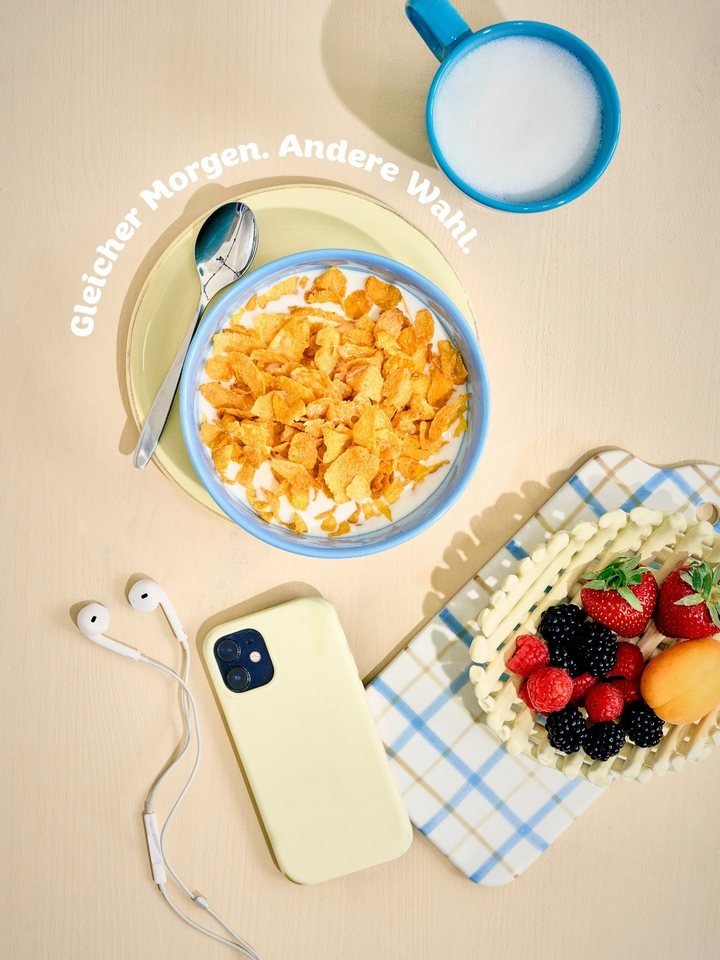 Cornflakes-Schale von oben mit Beeren und Smartphone, Schriftzug „Gleicher Morgen. Andere Wahl.“