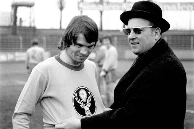 Historisches Pressefoto: ein Spieler im Trikot mit Hirsch-Emblem und ein Mann mit Hut am Spielfeldrand