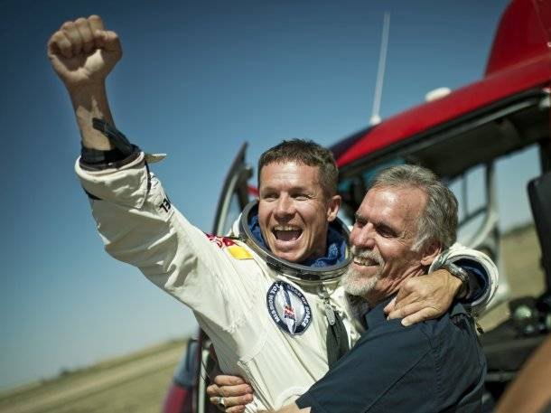 Felix Baumgartner im Druckanzug jubelt nach dem Stratos-Sprung, ein Teammitglied umarmt ihn