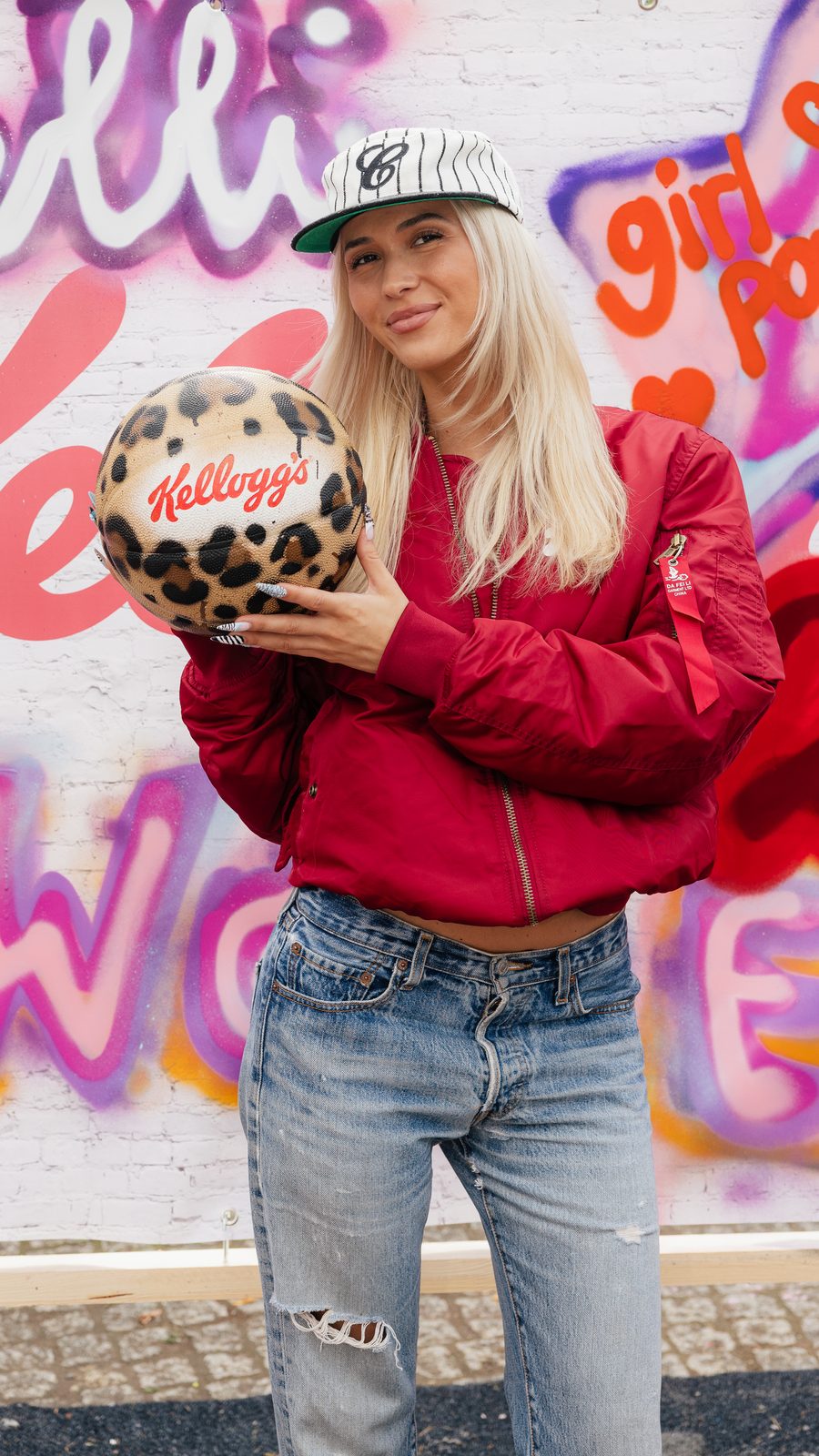Creatorin mit selbstgestaltetem Basketball vor einer Graffiti-Wand