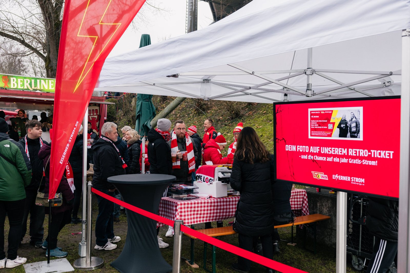 Fotostudio-Stand von Eiserner Strom vor der Alten Försterei mit Fans und Bildschirm „Dein Foto auf unserem Retro-Ticket“
