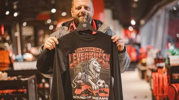 Fan hält im Fanshop ein schwarzes Sound-of-Dreams-Shirt mit Löwenmotiv hoch