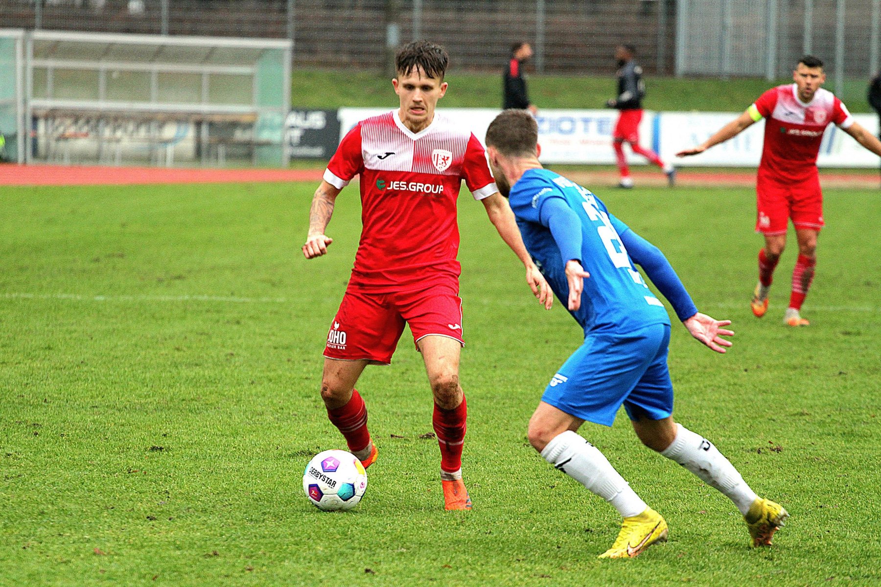 Zweikampf im Amateurfußball: Spieler im roten Trikot am Ball, ein Gegenspieler in Blau stellt sich ihm entgegen