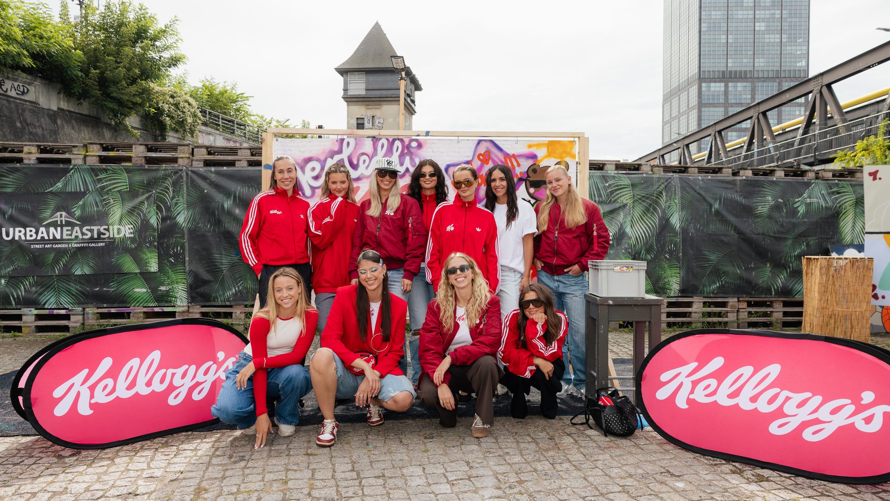 Gruppenfoto der Creatorinnen in roten Kellogg's-Jacken zwischen zwei Kellogg's-Beachflags im Berliner Hinterhof