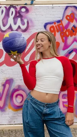 Creatorin in rot-weißem Shirt balanciert einen lila Kellogg’s-Basketball vor einer bunten Graffiti-Wand