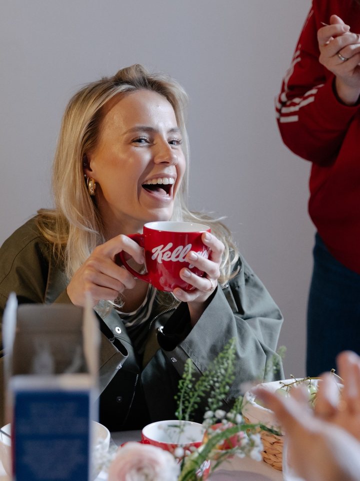 Lachende Frau mit Kellogg’s-Tasse am Frühstückstisch