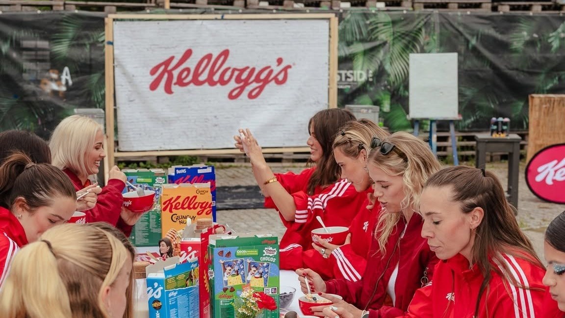 Lange Frühstückstafel mit Kellogg's-Schalen und -Packungen vor einem großen Kellogg's-Banner