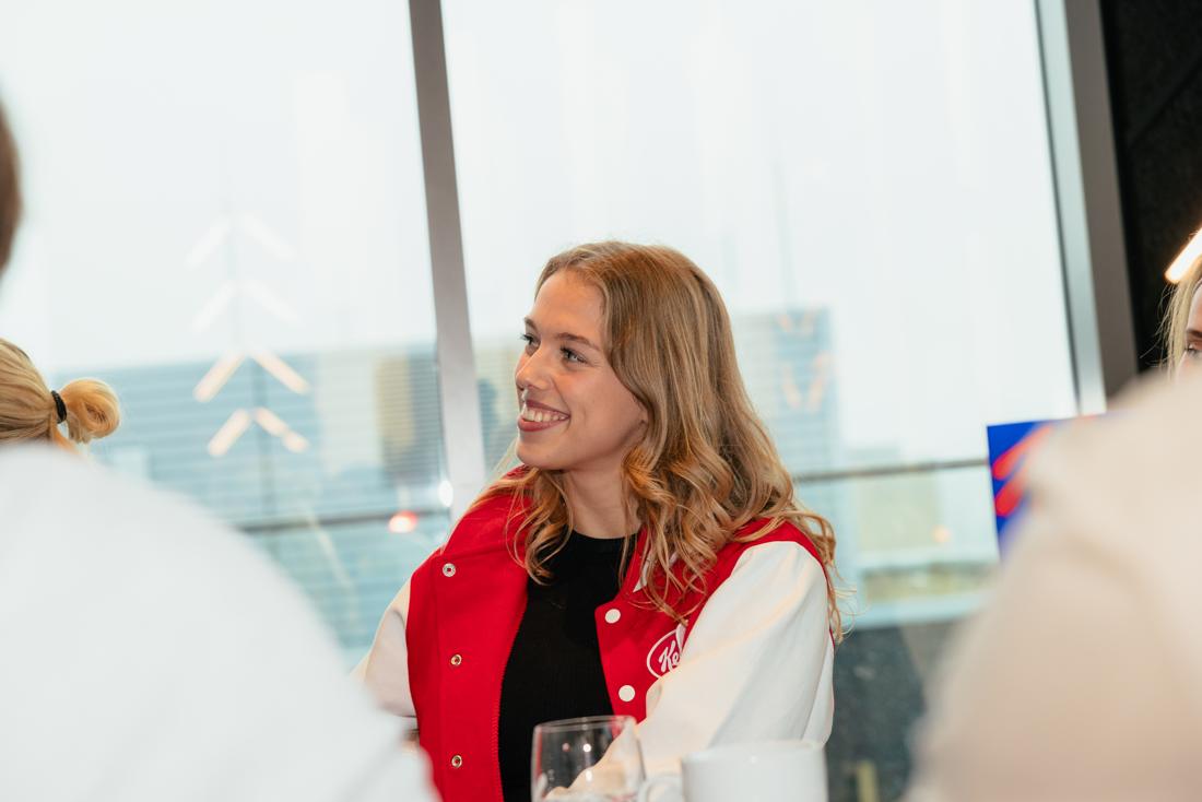 Creatorin in der roten Kellogg's-College-Jacke lacht beim Creator-Event vor Fensterfront/Skyline – warm, nahba